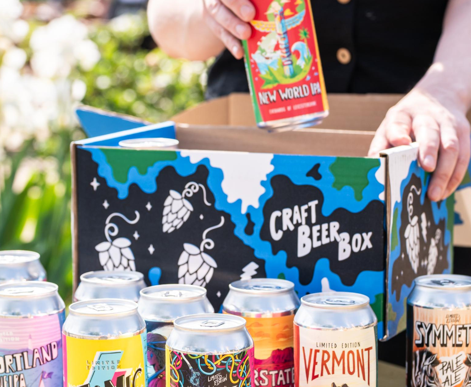 Assorted craft beer cans in front of a 'Craft Beer Box' with a person opening the box.
